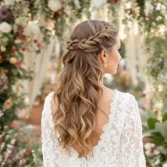 Eine Braut mit einer wunderschönen, geflochtenen Boho-Frisur steht vor einem üppigen Blumenbogen.