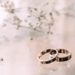 Zwei goldene Ringe liegen nebeneinander, ein Symbol für 23. hochzeitstag. Zarte Blüten im Hintergrund.