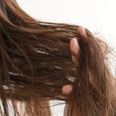 Eine Hand fährt durch braunes, strapaziertes Haar, das trocken und ungepflegt aussieht.