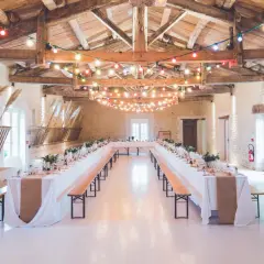 Festlich geschmückte Hochzeitsscheune mit langen Tafeln, Lichterketten und rustikalen Holzbänken.