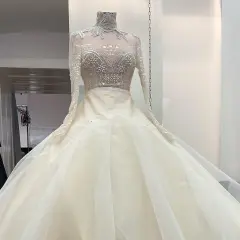 Ein prachtvolles, elfenbeinfarbenes Brautkleid mit einem hochgeschlossenen, bestickten Oberteil und einem voluminösen Tüllrock. Dieses Kleid könnte das Hochzeitskleid einer Kaiserin sein.
