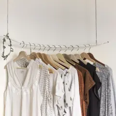 Eine Auswahl an Kleidungsstücken, die eine minimalistische capsule wardrobe bilden könnten, hängt an einer Garderobenstange.