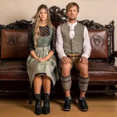 Ein junges Paar sitzt in traditioneller Tracht auf einer antiken Ledercouch. Sie sind bereit, in Tracht zu heiraten und zeigen stolz ihre festliche Kleidung.