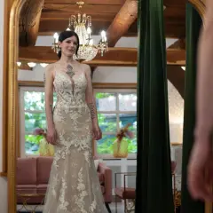 Braut steht vor Spiegel in einem figurbetonten Brautkleid mit Tüll und Spitze.