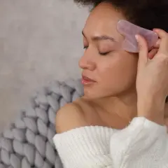 Frau mit Gua Sha Stein im Gesicht, um die Gua Sha Stein Wirkung zu erzielen.