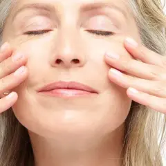 Frauenhände streicheln sanft über das Gesicht, ein Moment der Entspannung und Teil einer täglichen **Gesichtspflege Routine**.