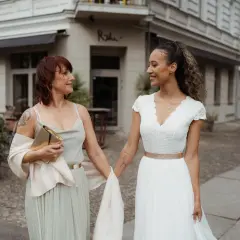 Brautmutterkleider mit Jacke: Eine Braut und ihre Mutter gehen Hand in Hand. Die Mutter trägt ein elegantes Kleid mit einer leichten Jacke.