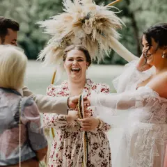 Lachende Menschen bei einer rituellen freien Trauung. Ein Paar hält bunte Seile, während Freunde zuschauen.