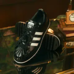 Schwarze Adidas Superstar Sneaker mit weißen Streifen, ein stilvolles Statement für aktuelle Sneaker Trends Herren. Schachfiguren und eine Spieluhr deuten auf eine strategische Eleganz hin.