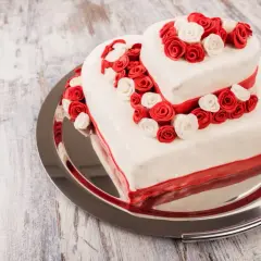 Ausgefallene Hochzeitstorte in Herzform, zweistöckig, mit roten und weißen Rosen verziert. Ein romantischer Hingucker für den besonderen Tag.