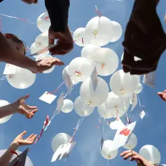 Gäste lassen bei einer Hochzeit weiße Luftballons mit Wünschen in den Himmel steigen.