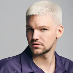 Mann mit platinblonden, kurz geschnittenen Haaren und einem Dreitagebart. Seine modernen herren frisuren unterstreichen seinen selbstbewussten Blick.