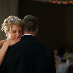 Ein zärtlicher Vater-Tochter-Tanz. Die Braut mit Diadem lehnt sich an ihren Vater, der einen schwarzen Anzug trägt.