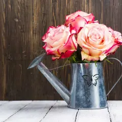 Ein Strauß Rosen in einer Gießkanne mit Schmetterlingsmotiv. Ein Symbol für 33 Jahre verheiratet, voller Liebe und Wachstum.