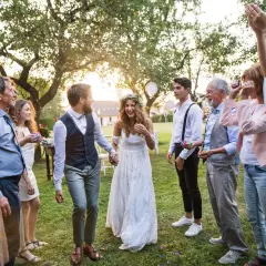Brautpaar feiert mit Familie und Freunden. Konfetti fliegt, die Stimmung ist ausgelassen. Eine fröhliche Hochzeit, bei der die Farben der Kleidung und des Konfettis im Sonnenlicht leuchten.