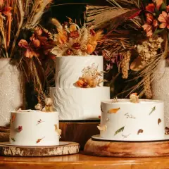 Drei weiße Hochzeitstorten, schlicht elegant dekoriert mit getrockneten Blumen und Blättern, umgeben von herbstlicher Deko.