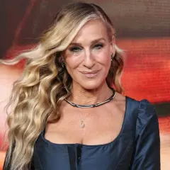 Sarah Jessica Parker mit ihrem charakteristischen beach waves bob, lächelnd in einem dunkelblauen Kleid.