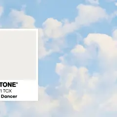 Pantone-Farbkarte "Cloud Dancer" vor einem Himmel mit Wolken. Diese zarte Farbe könnte die Farbe des Jahres 2026 sein.