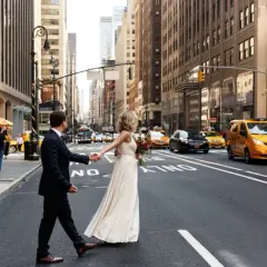 Ein Brautpaar hält Händchen und überquert eine belebte Straße in New York. Ein romantisches Bild für alle, die im Ausland heiraten möchten.