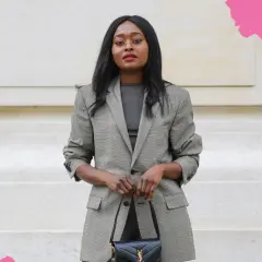 Frau in kariertem Blazer und dunklem Oberteil, perfekt für einen **business casual** Look, hält eine schwarze Handtasche.