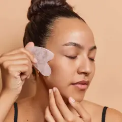 Frau mit geschlossenen Augen nutzt ein Gua Sha Stein für ihr Gesicht.