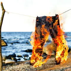 Jeans brennen am Strand, ein Symbol für den Polterabend. Die Flammen tanzen, während die Wellen rauschen.