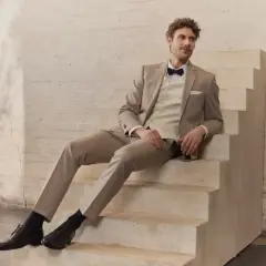 Mann in hellem Hochzeitsanzug mit Fliege sitzt auf Treppe. Perfekt für die Frage: wann Hochzeitsanzug kaufen?