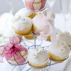Zarte Muffins mit weißer Glasur, Blüten und Perlen, dekoriert mit rosa Bändern, perfekt für eine Hochzeit.