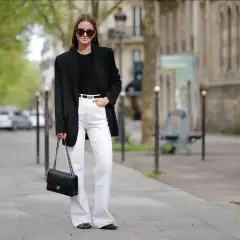 Frau in schicker Business-Kleidung mit schwarzem Blazer, weißer Hose und Chanel-Tasche.