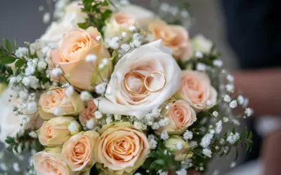 Ein Hochzeitsstrauß mit Pfirsichrosen und Schleierkraut, darin zwei goldene Ringe. Ein Symbol für 27 Jahre verheiratet.