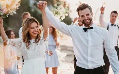 Glückliches Brautpaar feiert seine low budget hochzeit am Strand. Die Braut hält einen Blumenstrauß, der Bräutigam strahlt.
