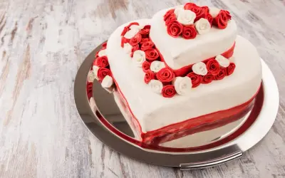 Ausgefallene Hochzeitstorte in Herzform, zweistöckig, mit roten und weißen Rosen verziert. Ein romantischer Hingucker für den besonderen Tag.
