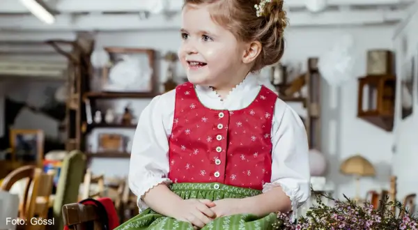 Ein fröhliches Mädchen im Dirndl mit einer hübschen Schleife im Haar. Die Tracht ist für Kinder perfekt.