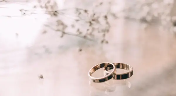 Zwei goldene Ringe liegen nebeneinander, ein Symbol für 23. hochzeitstag. Zarte Blüten im Hintergrund.
