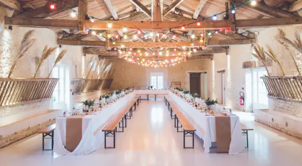 Festlich geschmückte Hochzeitsscheune mit langen Tafeln, Lichterketten und rustikalen Holzbänken.