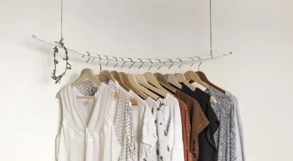 Eine Auswahl an Kleidungsstücken, die eine minimalistische capsule wardrobe bilden könnten, hängt an einer Garderobenstange.