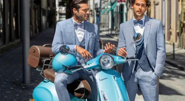 Zwei stilvolle Männer in hellblauen Anzügen, perfekt für einen Hochzeit Gast, posieren auf einer türkisfarbenen Vespa.
