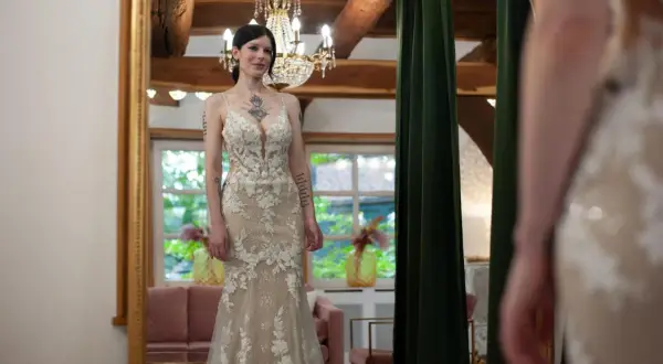 Braut steht vor Spiegel in einem figurbetonten Brautkleid mit Tüll und Spitze.