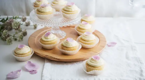 Zarte Cupcakes mit cremiger Glasur und rosa Blütenblättern – süße Ideen für eine Hochzeit.