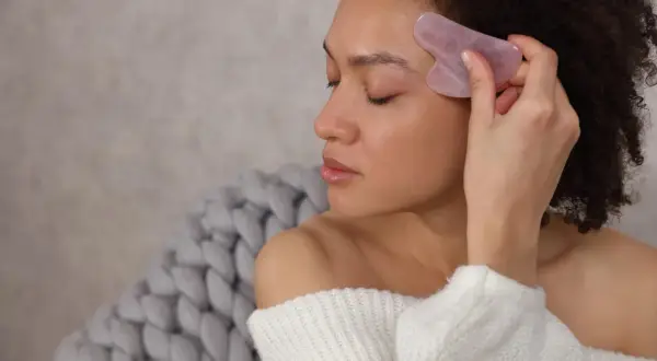Frau mit Gua Sha Stein im Gesicht, um die Gua Sha Stein Wirkung zu erzielen.