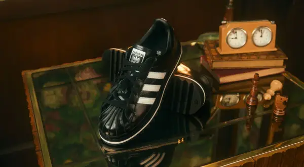 Schwarze Adidas Superstar Sneaker mit weißen Streifen, ein stilvolles Statement für aktuelle Sneaker Trends Herren. Schachfiguren und eine Spieluhr deuten auf eine strategische Eleganz hin.