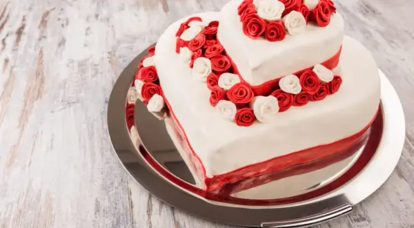 Ausgefallene Hochzeitstorte in Herzform, zweistöckig, mit roten und weißen Rosen verziert. Ein romantischer Hingucker für den besonderen Tag.