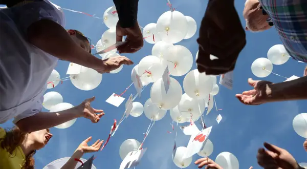 Gäste lassen bei einer Hochzeit weiße Luftballons mit Wünschen in den Himmel steigen.