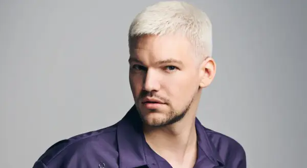 Mann mit platinblonden, kurz geschnittenen Haaren und einem Dreitagebart. Seine modernen herren frisuren unterstreichen seinen selbstbewussten Blick.
