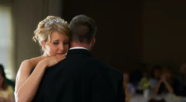 Ein zärtlicher Vater-Tochter-Tanz. Die Braut mit Diadem lehnt sich an ihren Vater, der einen schwarzen Anzug trägt.