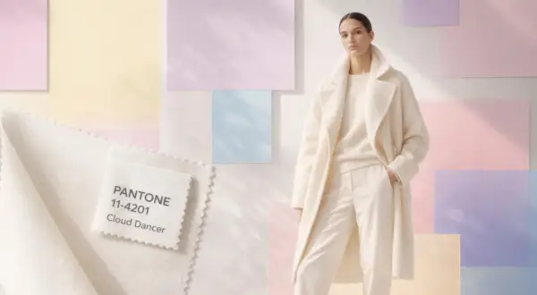 Ein Model trägt ein cremefarbenes Outfit vor pastellfarbenen Hintergründen. Ein Stoffmuster zeigt die Pantone Farbe des Jahres: Cloud Dancer.