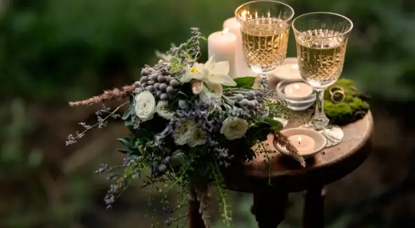 Romantische Szene mit Blumenstrauß, zwei Gläsern Sekt und Kerzenlicht. Ein Ring auf Moos deutet auf einen besonderen Anlass hin, vielleicht den 31. Hochzeitstag.