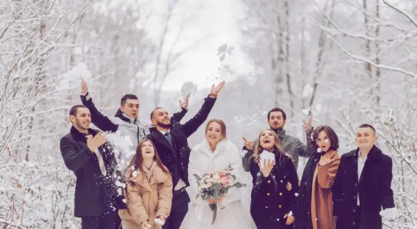 Brautpaar und Gäste werfen im Winter Schnee. Eine standesamtliche Hochzeit im Schnee mit fröhlichen Gästen.
