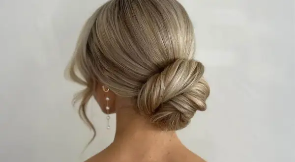 Elegante Hochzeitsfrisur mit einem kunstvoll gedrehten Dutt und zarten Perlenohrringen. Perfekt für den großen Tag.