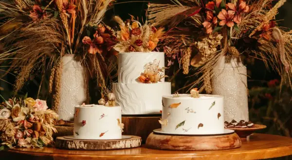 Drei weiße Hochzeitstorten, schlicht elegant dekoriert mit getrockneten Blumen und Blättern, umgeben von herbstlicher Deko.